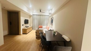 A modern living room with a sofa, a dining table, and a TV mounted on the wall.