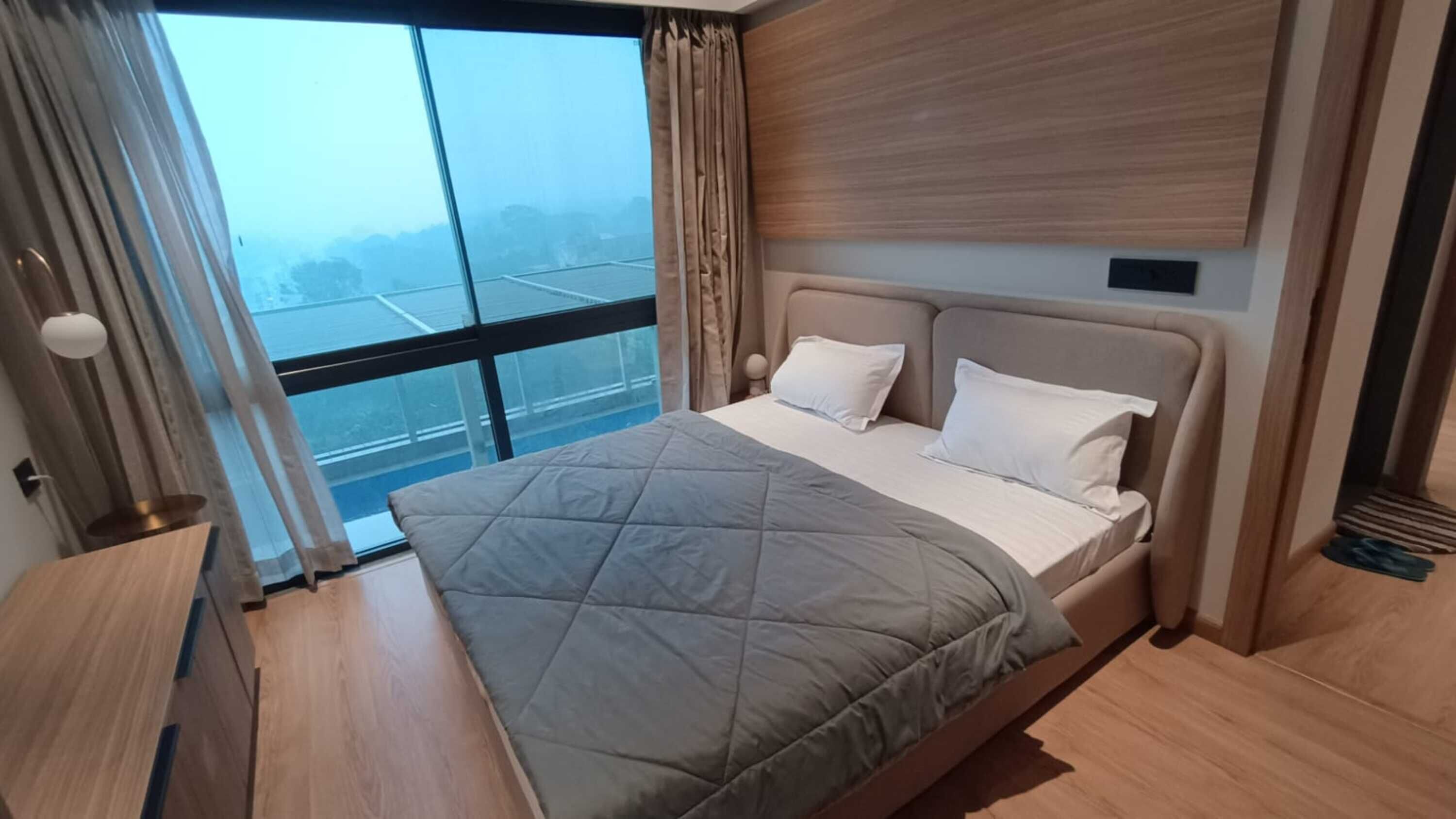 Een moderne slaapkamer met een groot bed, een houten nachtkastje en uitzicht door een groot raam.