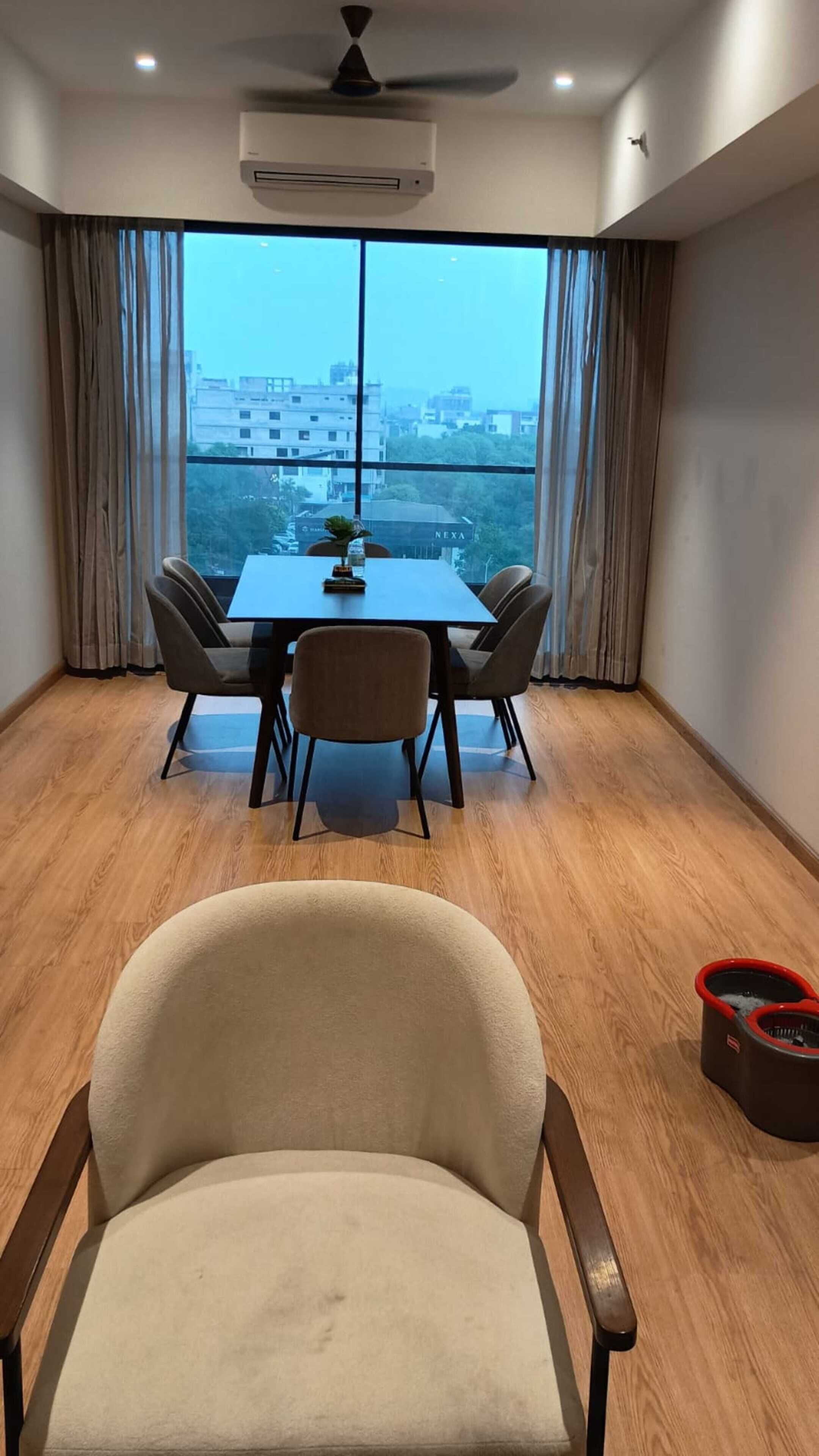 Een kamer met een eettafel, vier stoelen, een plafondventilator en een uitzicht op gebouwen door grote ramen.