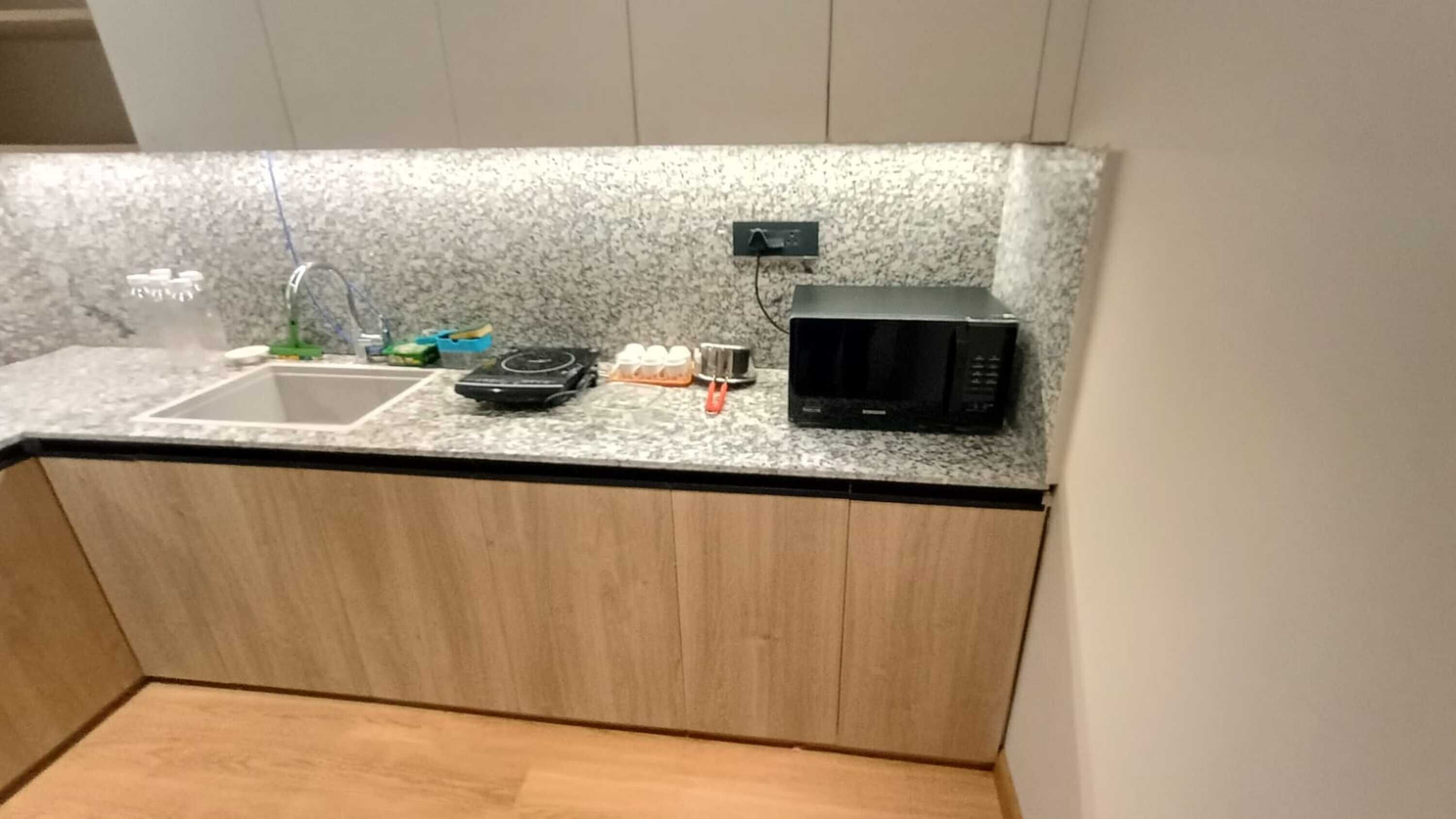 Een keuken met een granieten aanrecht, een spoelbak, een magnetron en een klein elektrisch fornuis.
