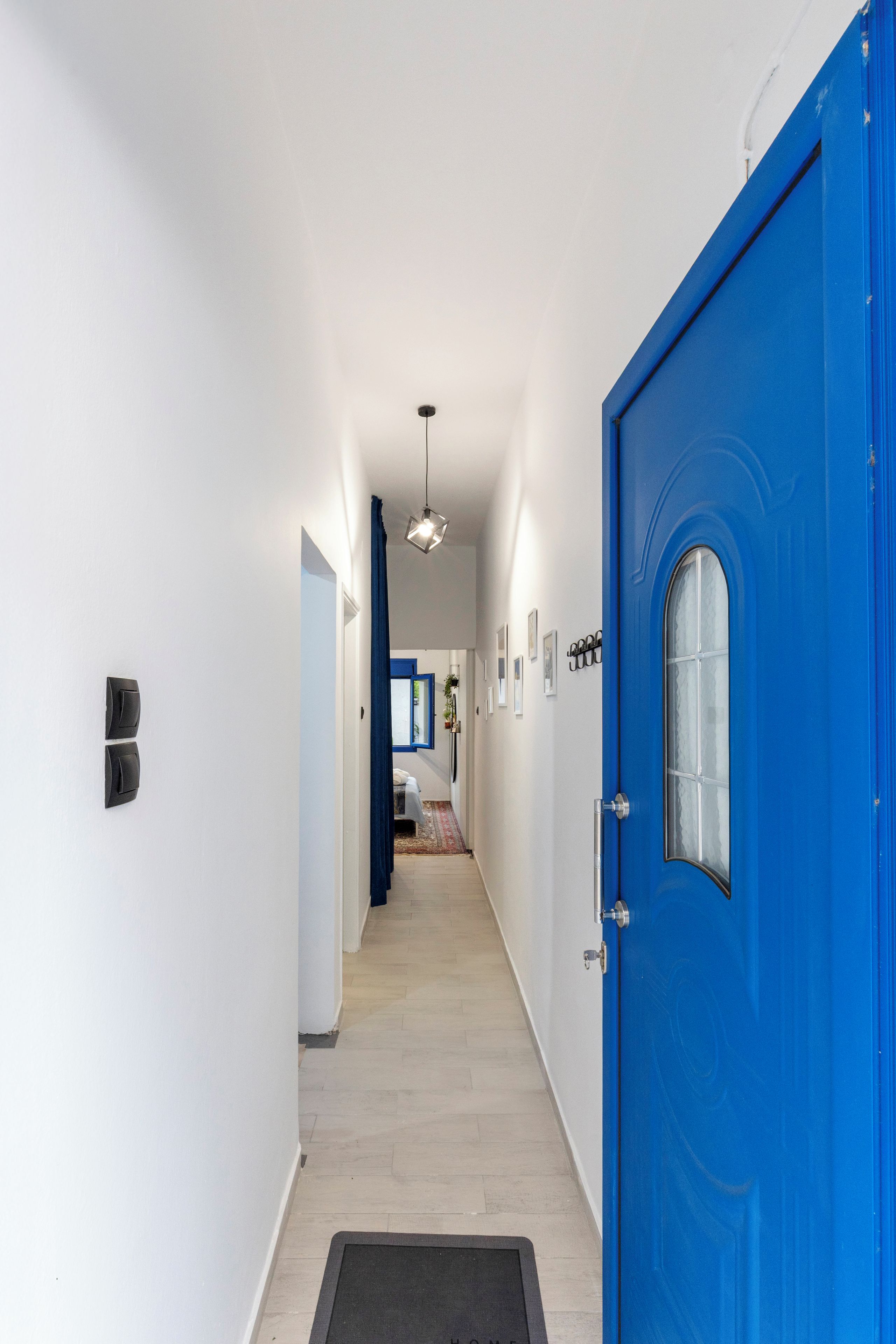 A hallway with a blue door, a light fixture, and a bed in the distance.
