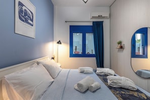 A hotel room with a bed, a bedside lamp, a window with curtains, a wall-mounted air conditioner, and a framed artwork.