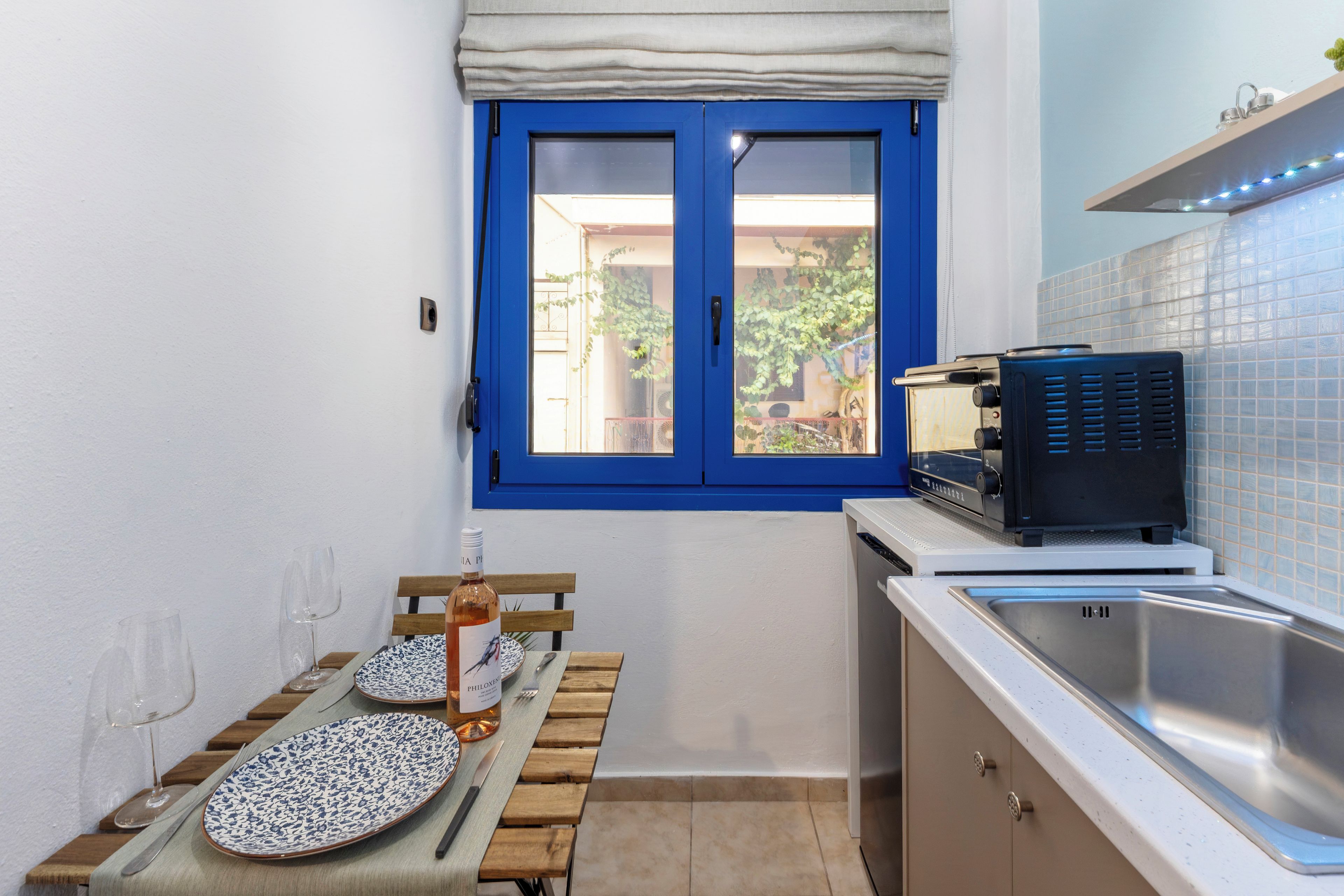 A compact kitchen with a blue-framed window, a sink, and a countertop with a coffee machine.