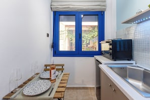 A compact kitchen with a blue-framed window, a sink, and a countertop with a coffee machine. - Διαμέρισμα στο κέντρο της πόλης. (Filippiada)