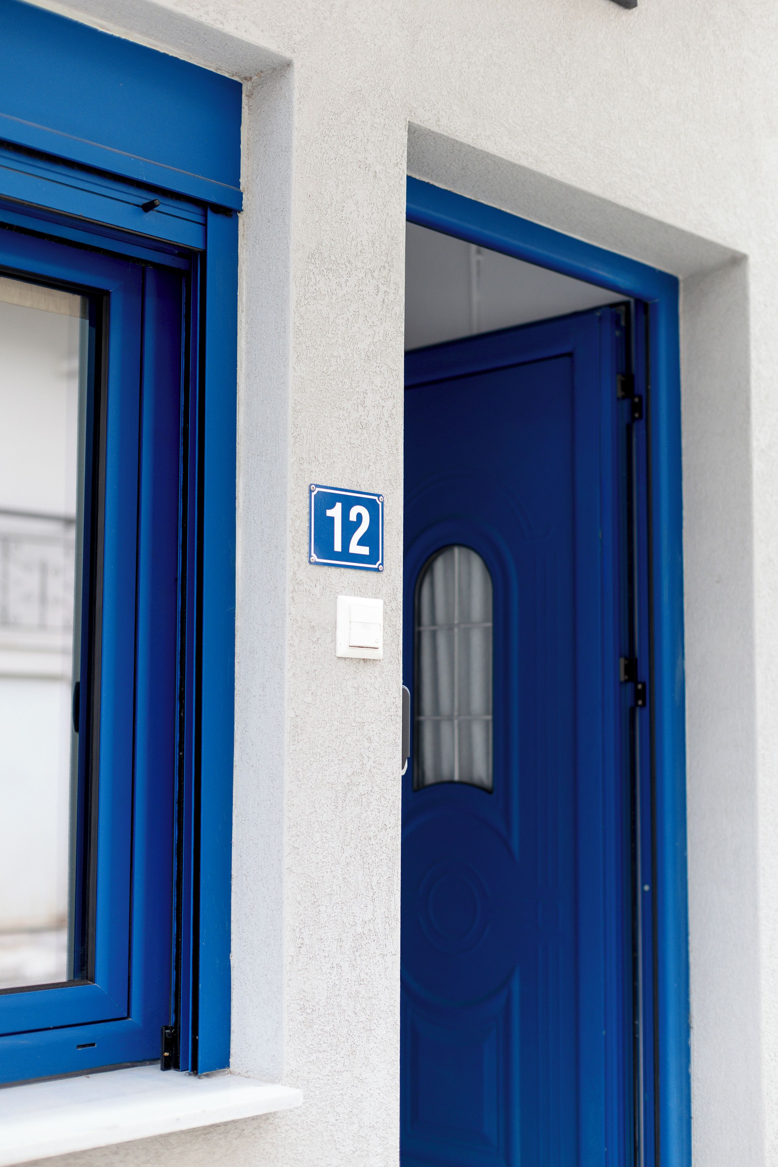 A blue door with a number '12' sign above it, a window with blue trim, and a white wall.