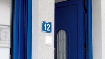 A blue door with a number '12' sign above it, a window with blue trim, and a white wall.