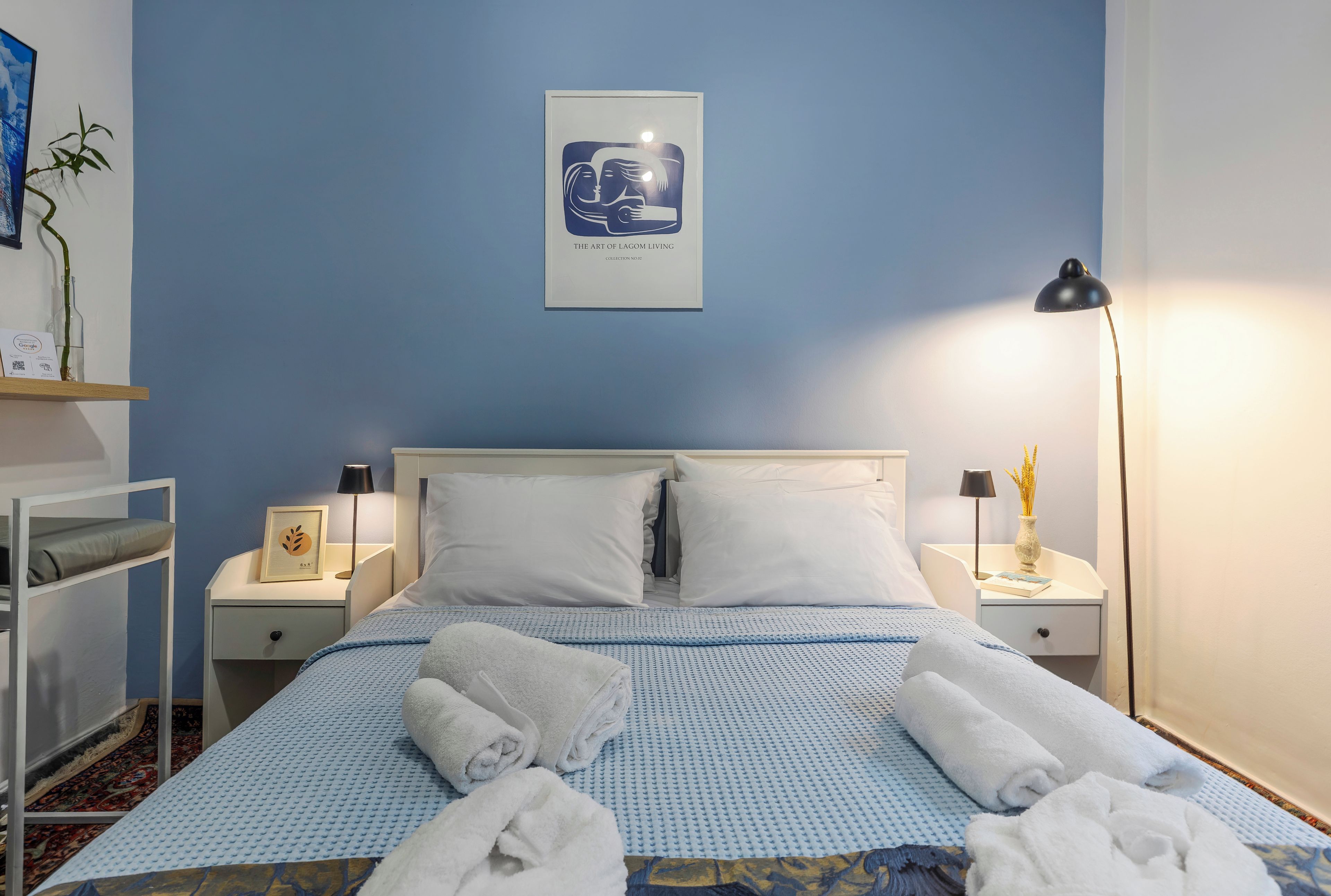 Una camera d'albergo con un letto, due comodini, una lampada, un'opera d'arte incorniciata e una piccola pianta.