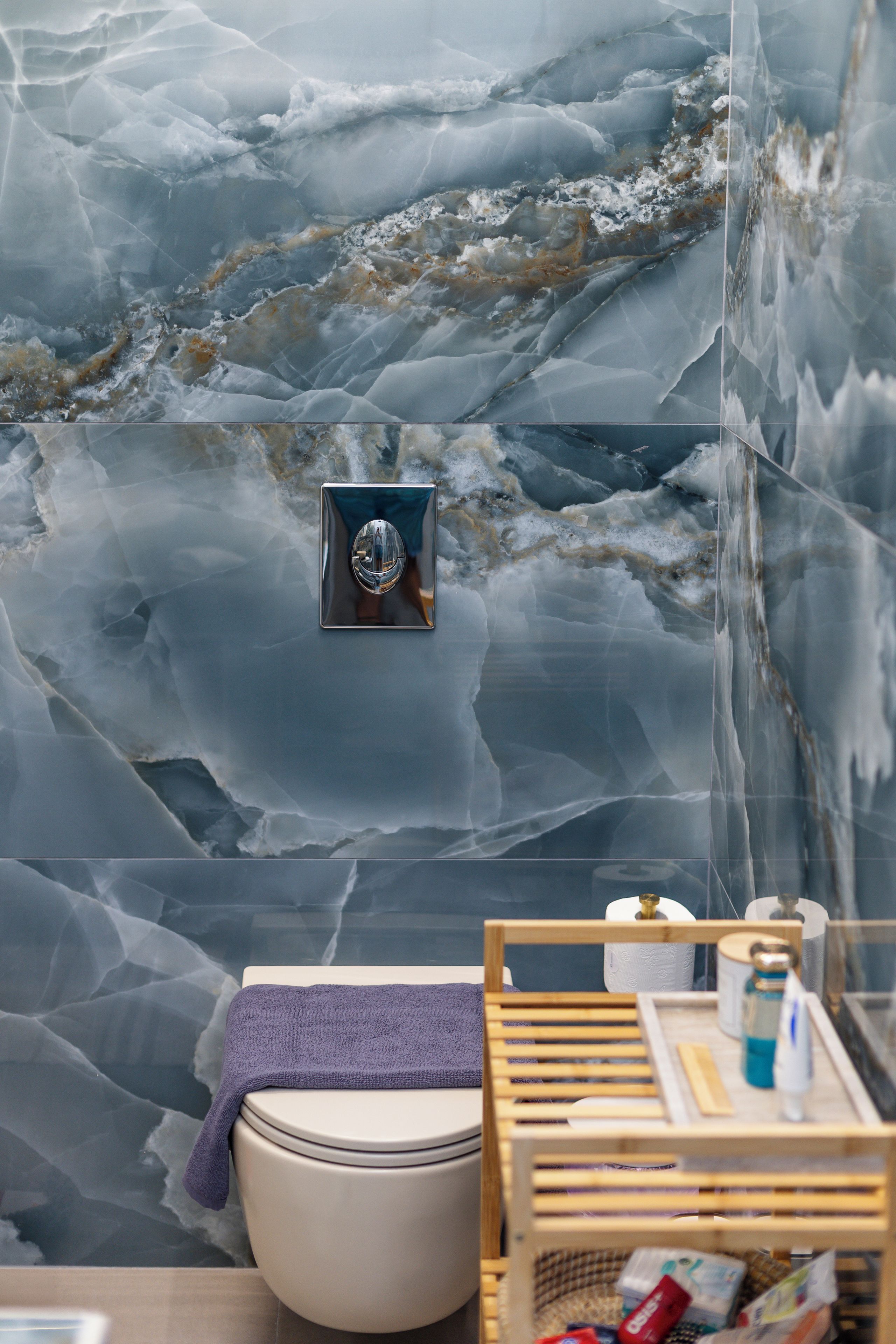 Un bagno con parete in marmo, un water, uno scaffale di legno con articoli da toilette e un asciugamano.