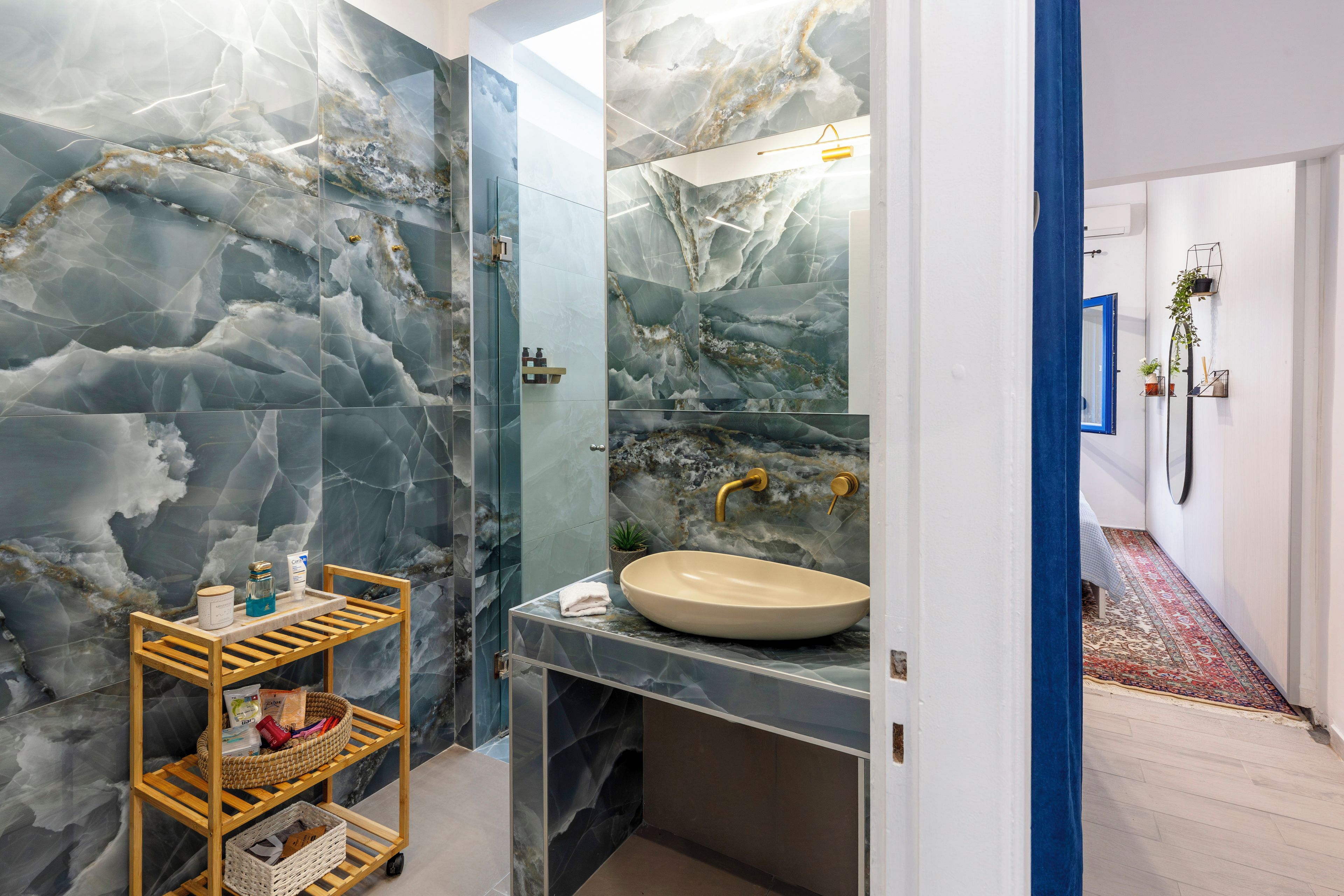A bathroom with a marble wall, a wooden shelf with toiletries, a sink, and a mirror.