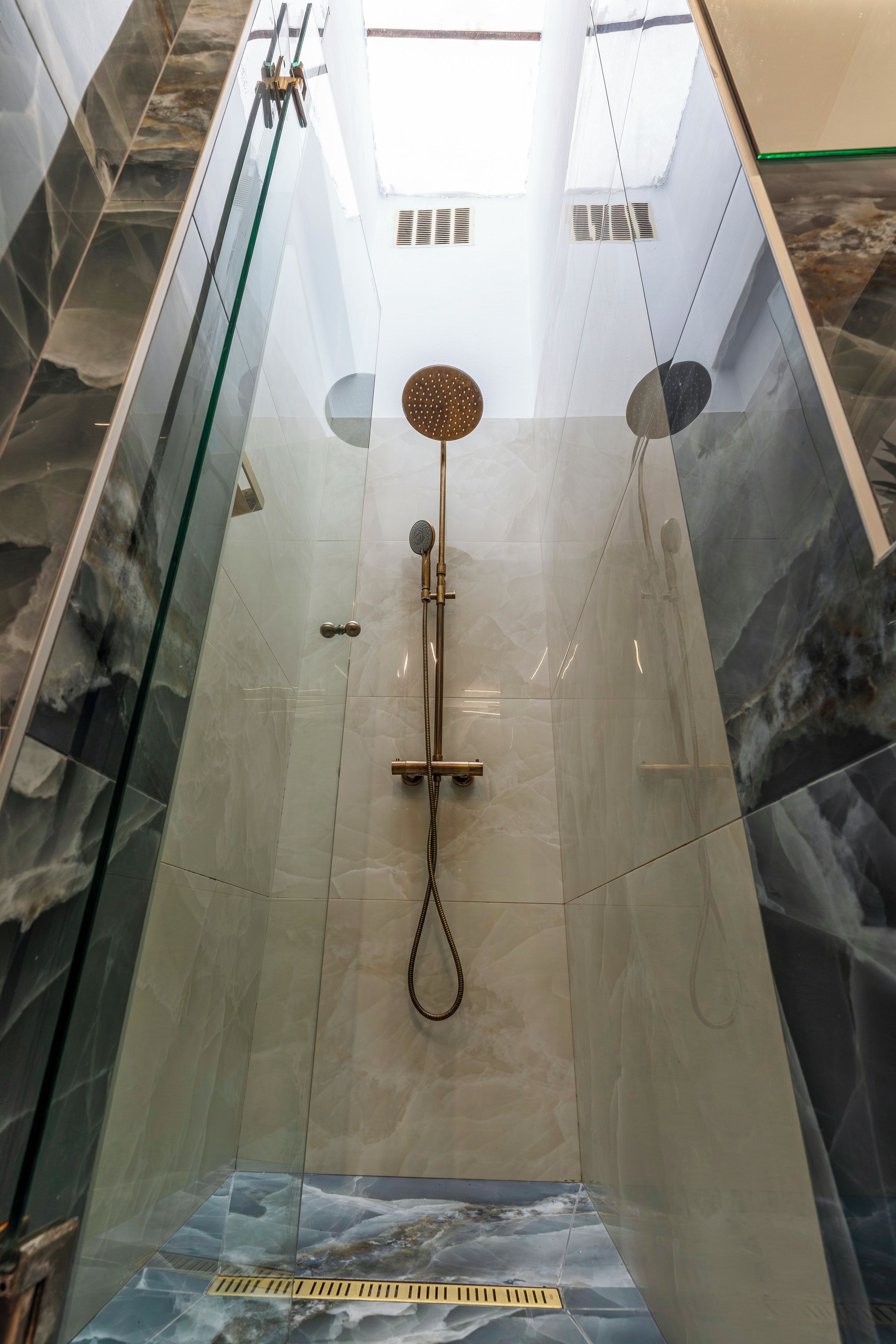 A glass-enclosed shower with a handheld showerhead, a wall-mounted faucet, and a floor drain.
