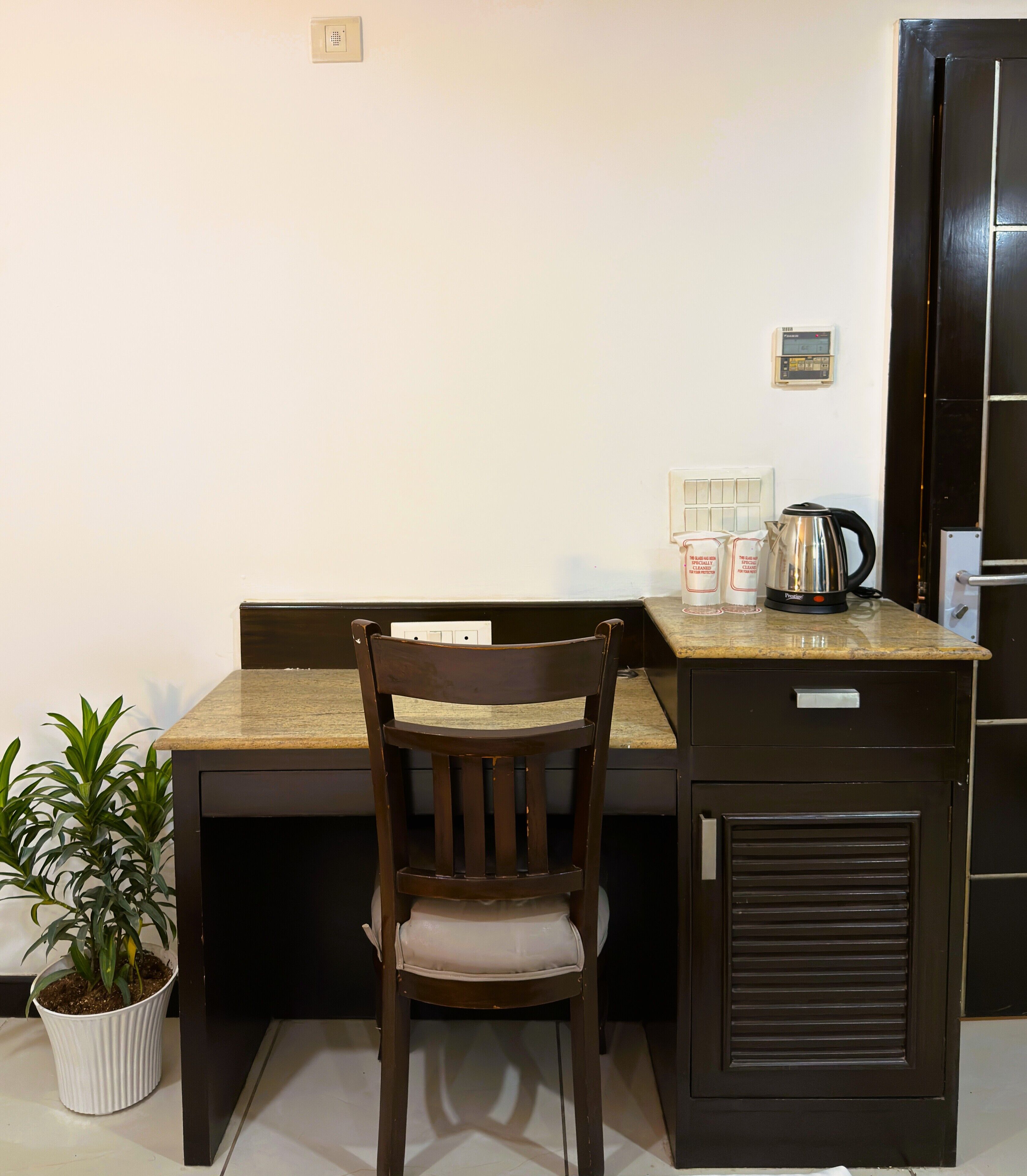 Una kitchenette pequeña con una silla de madera, una planta en maceta y una cafetera sobre la encimera.