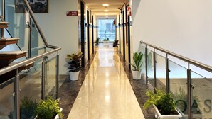 A modern hotel corridor with a glass railing, potted plants, and a fire exit sign. - Hotel Oasis One (Gurugram)