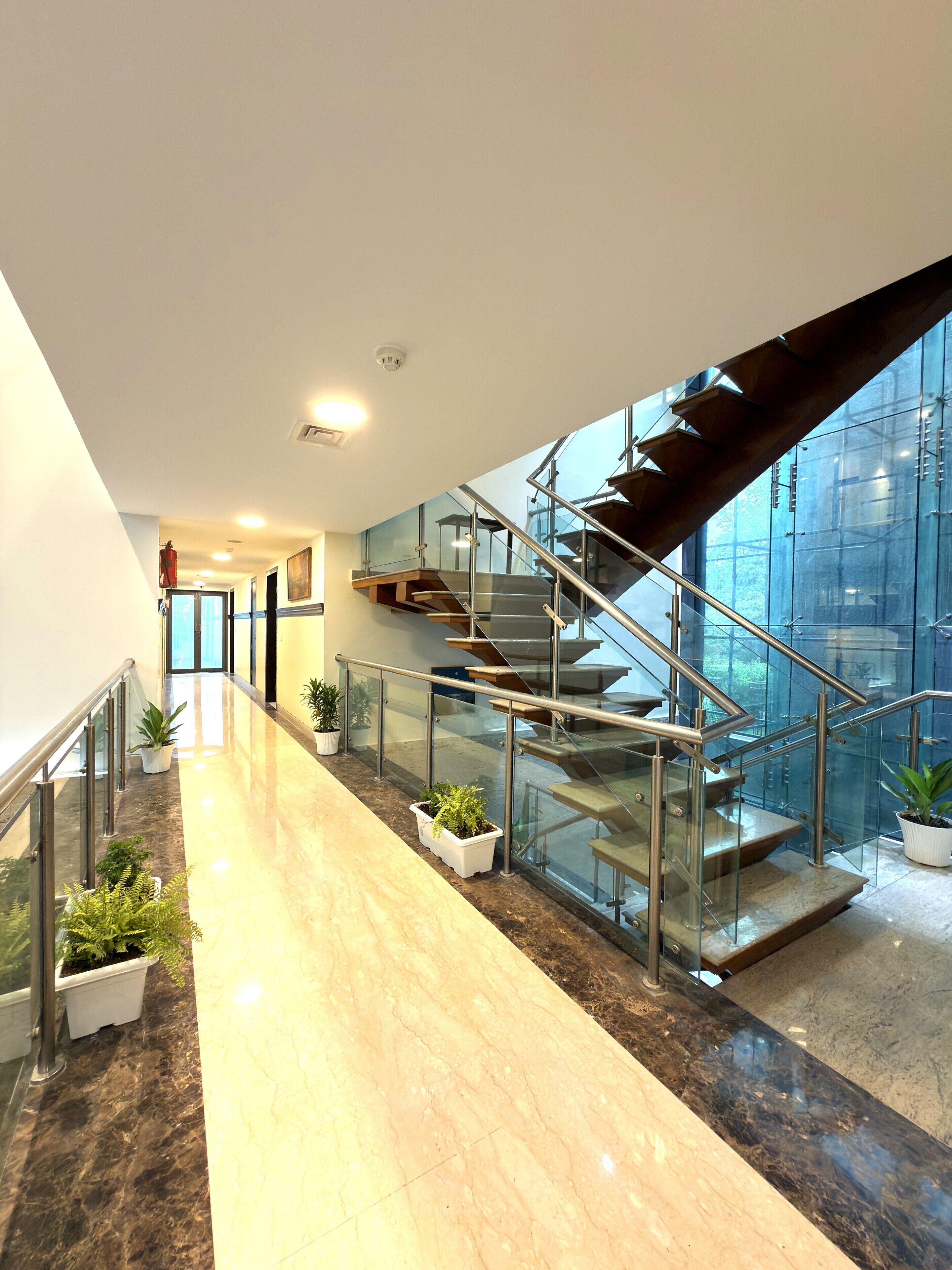 A modern interior with a glass staircase, marble flooring, and potted plants.