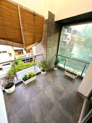 En balkon med plantekasser, udsigt til en bygning og en strukturvæg.
