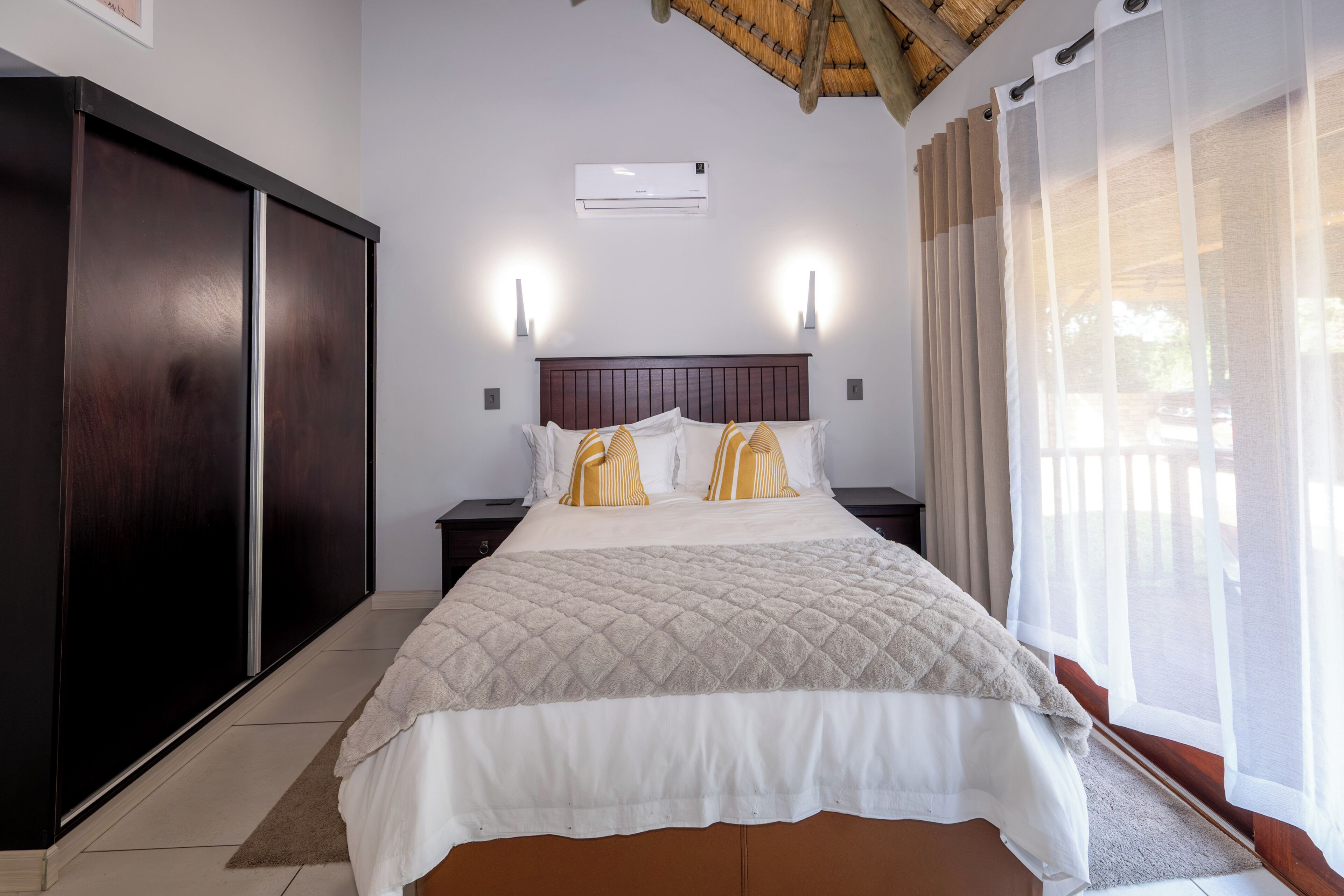 A hotel room with a large bed, two bedside tables, a wardrobe, a ceiling fan, and a window with curtains.
