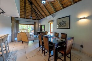 A spacious dining area with a high ceiling and a thatched roof, a television, and a framed artwork on the wall. - Kruger 531 Luxury Double Storey Chalet (Hazyview)