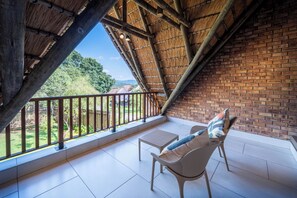 A balcony with a view of a brick wall and greenery, furnished with a chair and a small table. - Kruger 531 Luxury Double Storey Chalet (Hazyview)