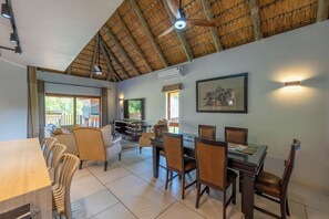 A dining area with a table and chairs, a ceiling fan, and a television. - Kruger 531 Luxury Double Storey Chalet (Hazyview)