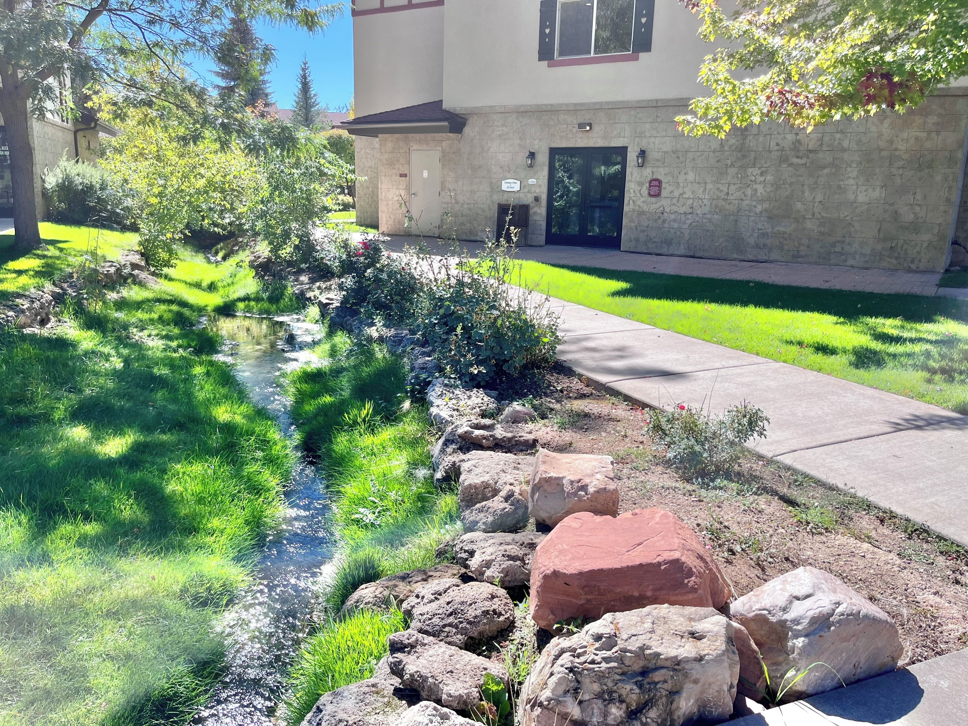 A landscaped garden with a small stream, a stone wall, and a building with a door and windows.