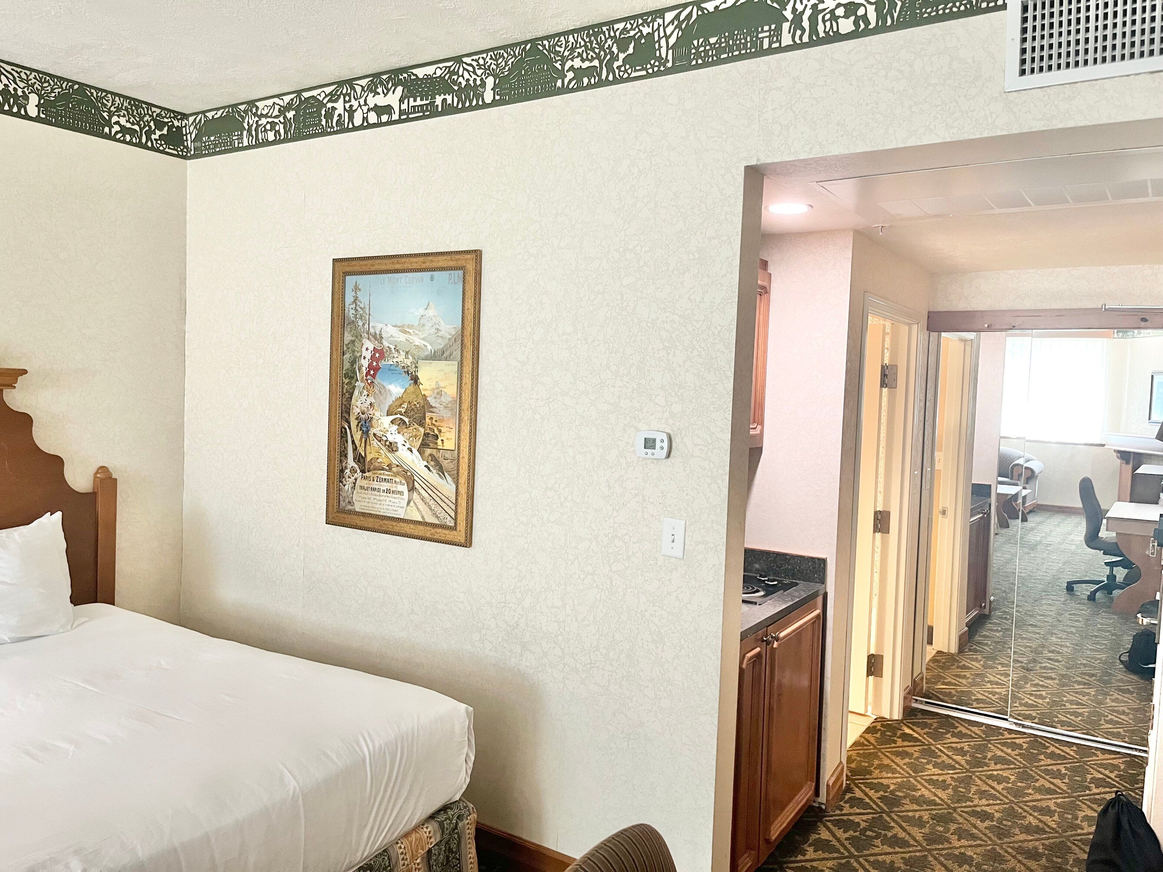 Une chambre d’hôtel avec un lit, un tableau, un bureau et une vue sur le couloir.