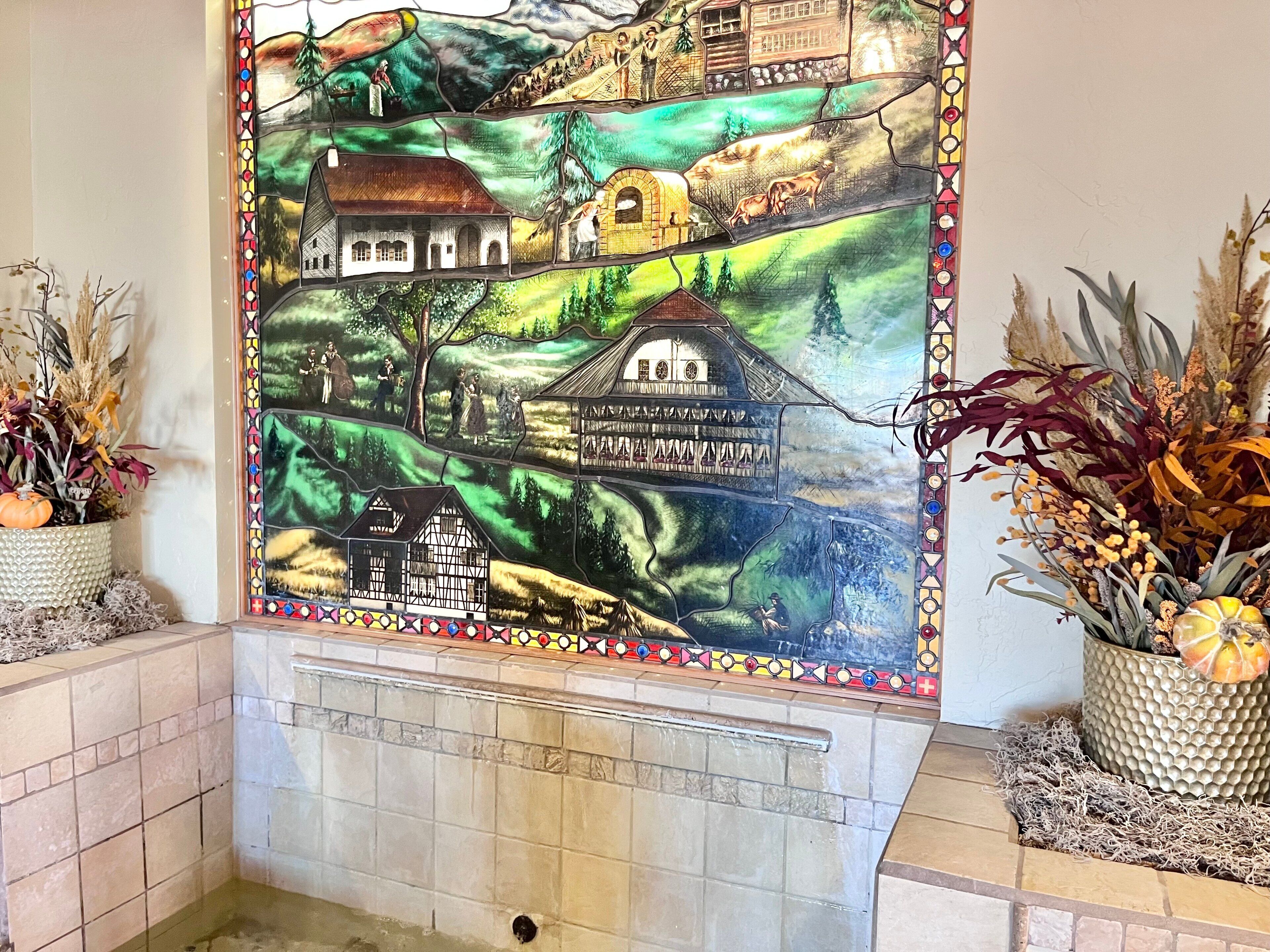 A stained glass window depicting a rural landscape with houses and people.