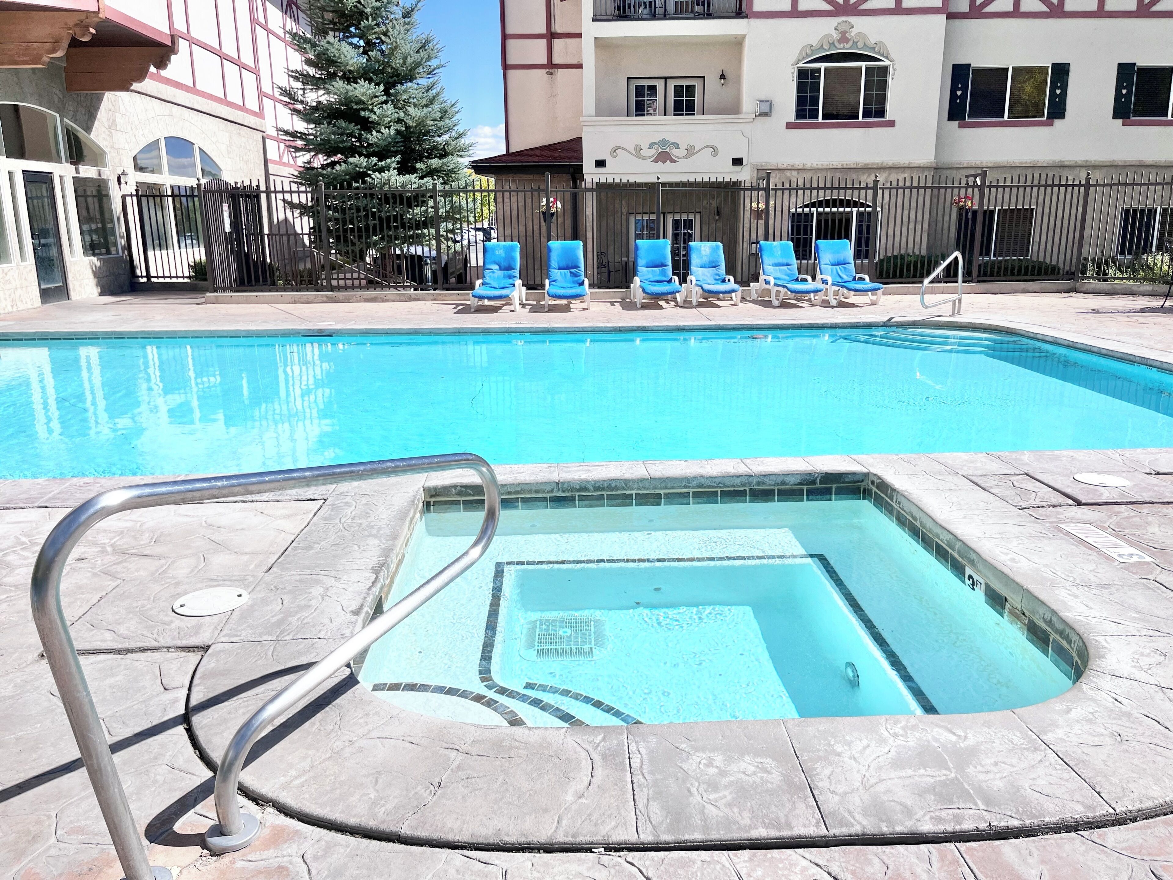 Une piscine avec un petit jacuzzi, entourée de chaises longues et d’une clôture.