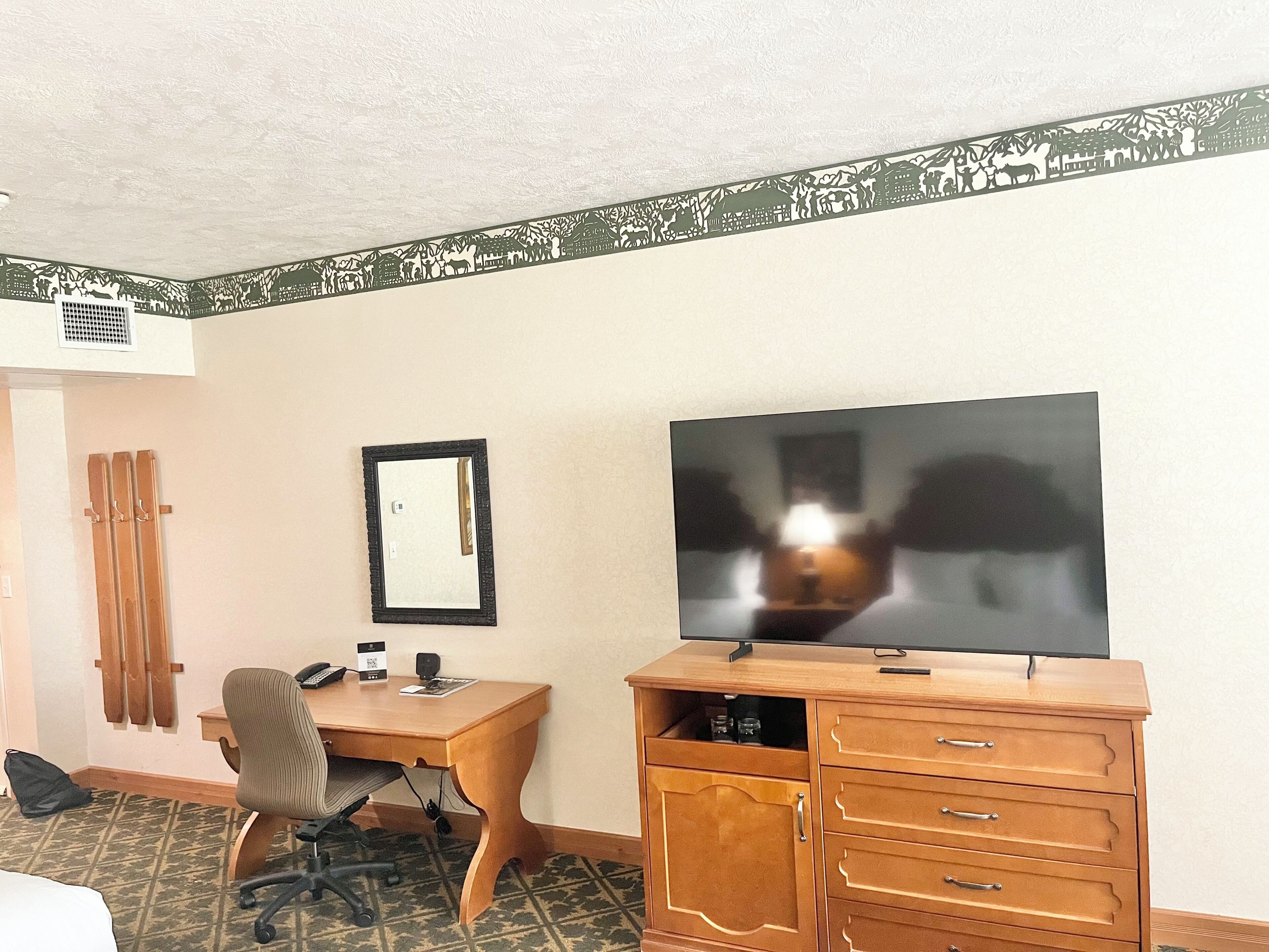 A hotel room with a wooden desk, a chair, a television, and a wardrobe.