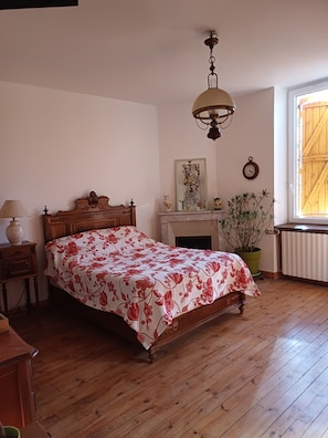 Un dormitorio con una cama de madera, una mesita de noche, un espejo, un reloj, una ventana con vistas y una planta en maceta.