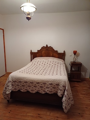 Una cama individual con edredón floral, cabecera de madera y mesita de noche con lámpara.