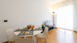 Een ontbijtruimte met een tafel, een televisie en een groot raam met gordijnen.