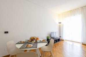Ein Essbereich mit Tisch, gedecktem Frühstück, einem Fernseher und einem großen Fenster mit Vorhängen.