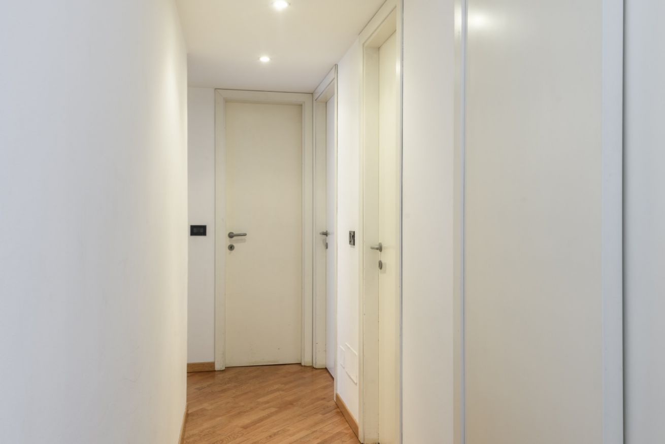 A narrow hallway with wooden flooring and white walls, leading to a closed door.