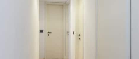 Un pasillo estrecho con suelo de madera y paredes blancas, que conduce a una puerta cerrada.