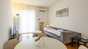 Een moderne hotelkamer met een bed, een eettafel, een stoel, een lamp en een schilderij aan de muur.