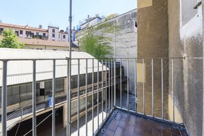 Ein Balkon mit Metallgeländern, der auf ein Gebäude mit einem Ziegeldach blickt.