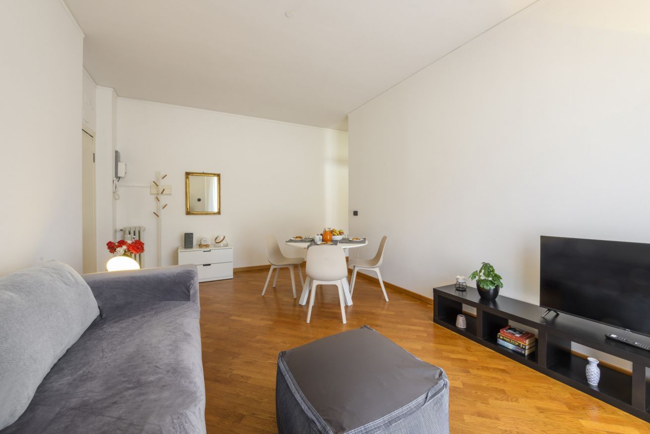 A living room with a sofa, ottoman, TV, and a dining area with chairs and a table.