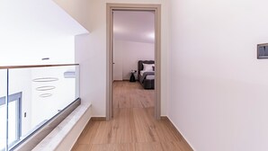 Ein schmaler Korridor mit Holzboden führt zu einem Schlafzimmer mit Bett und Nachttisch.