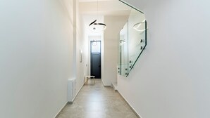 Un couloir moderne avec un mur en verre, une porte au fond et une petite table avec une chaise.