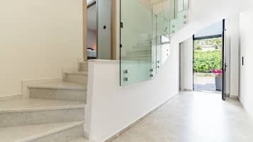 A modern interior with a marble staircase, glass railings, and a view of a garden.