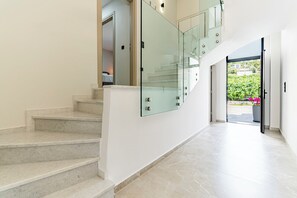 Un intérieur moderne avec un escalier en marbre, des rampes de protection en verre et une vue sur un jardin.