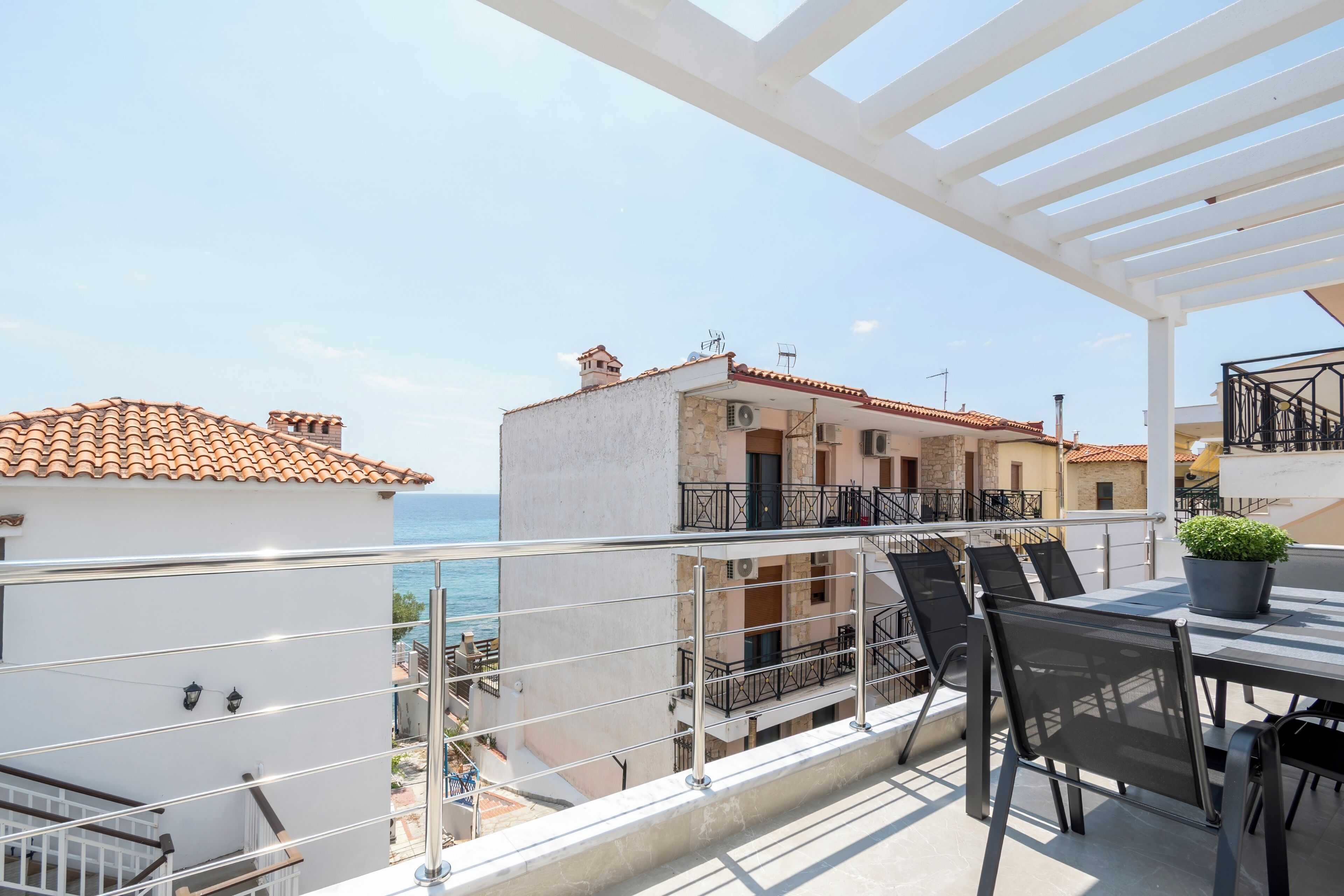 Ein Balkon mit Tisch und Stühlen, der auf eine Küstenlandschaft mit Gebäuden und dem Meer blickt.