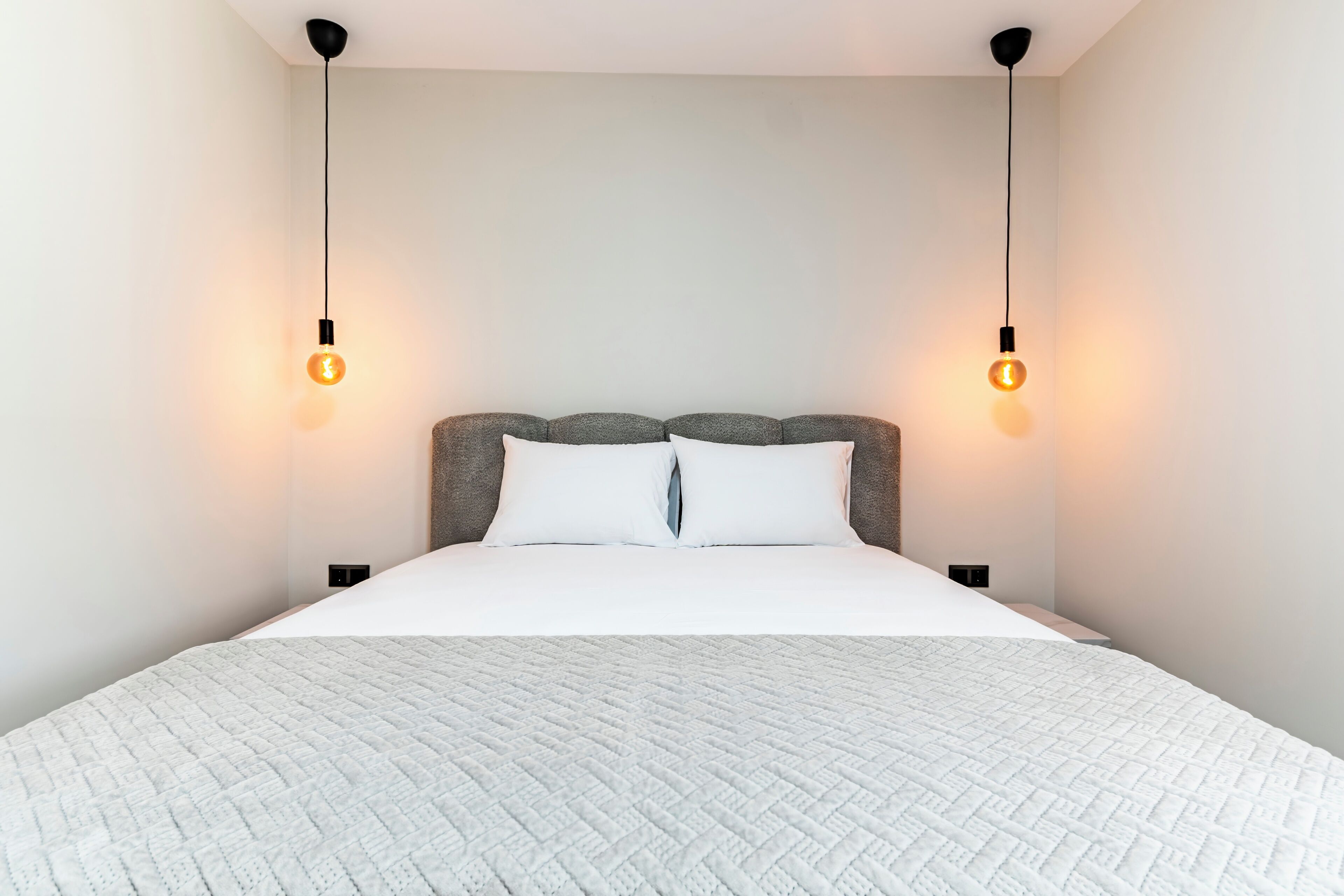 A modern bedroom with a large bed, two bedside lamps, and a plain wall.