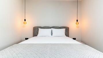 A modern bedroom with a large bed, two bedside lamps, and a plain wall.