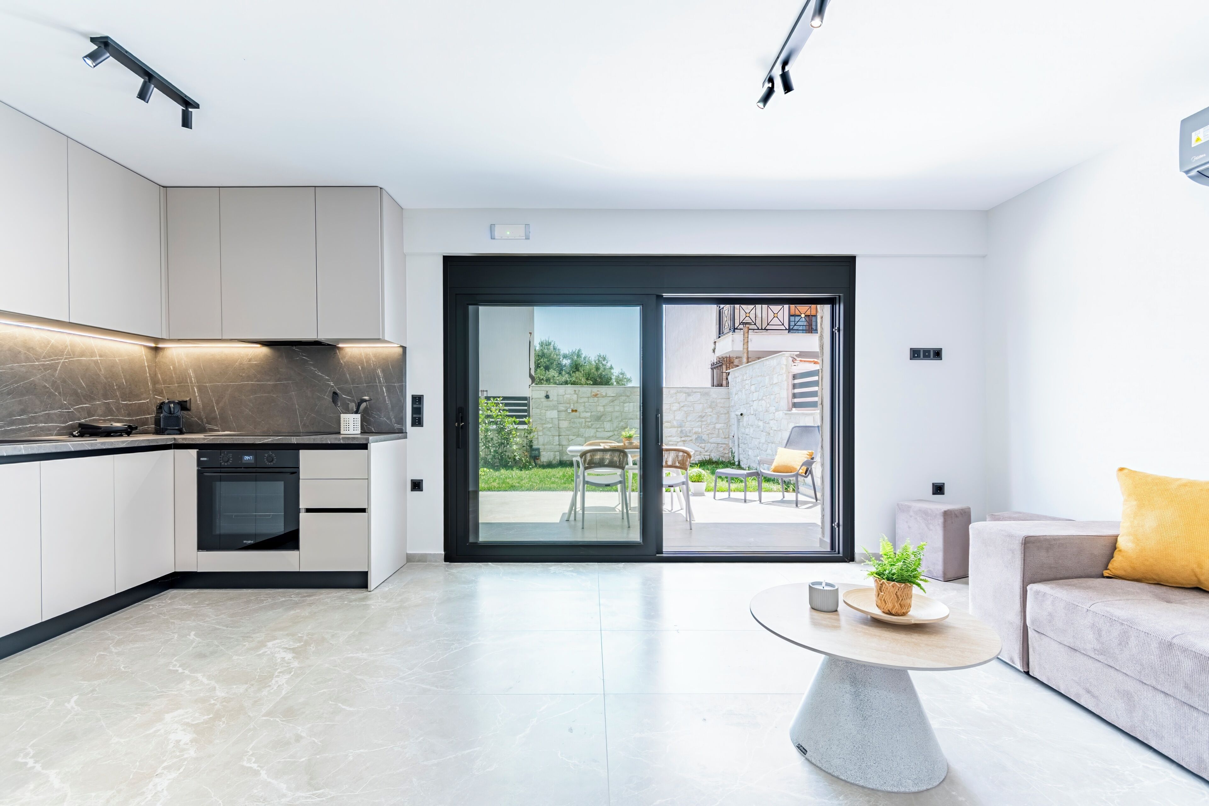 A modern kitchen with integrated appliances, a dining area with a round table, and a sliding glass door leading to an outdoor patio.
