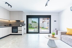 Une cuisine moderne dotée d’appareils électroménagers intégrés, un coin repas avec une table ronde et une porte-fenêtre coulissante donnant sur une terrasse extérieure.