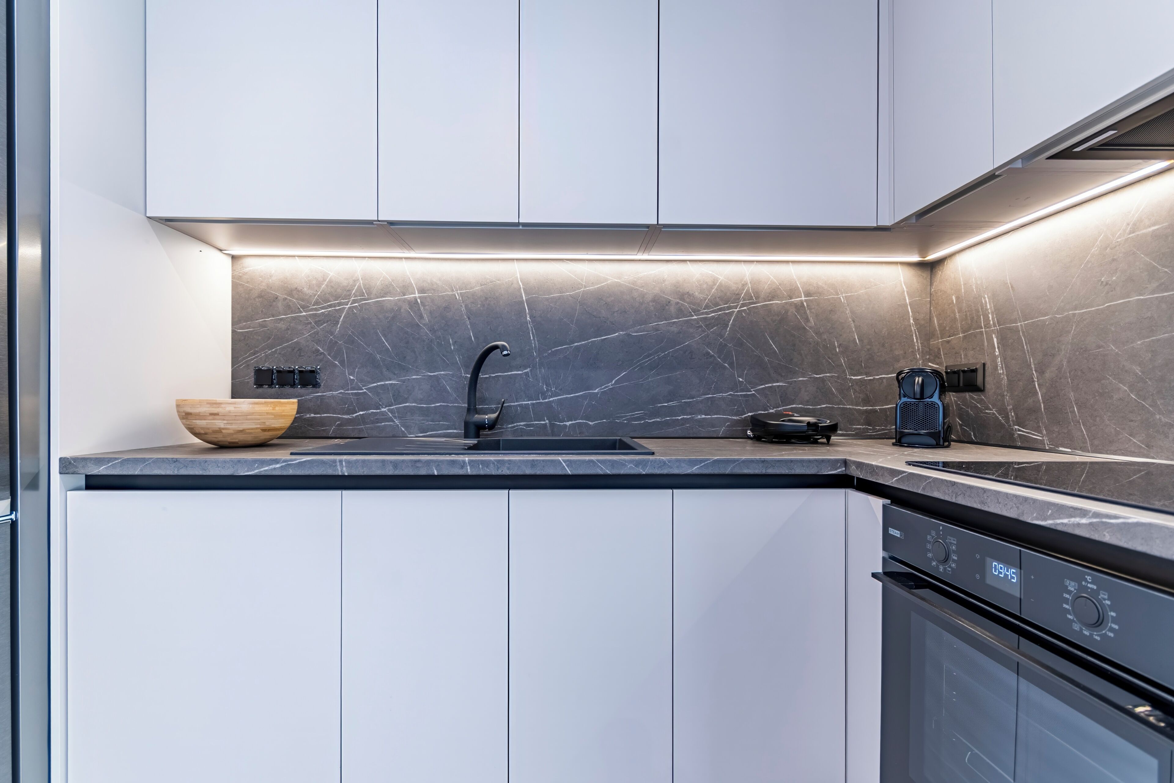 A modern kitchen with a sleek black faucet, a wooden bowl on the counter, and a coffee machine.