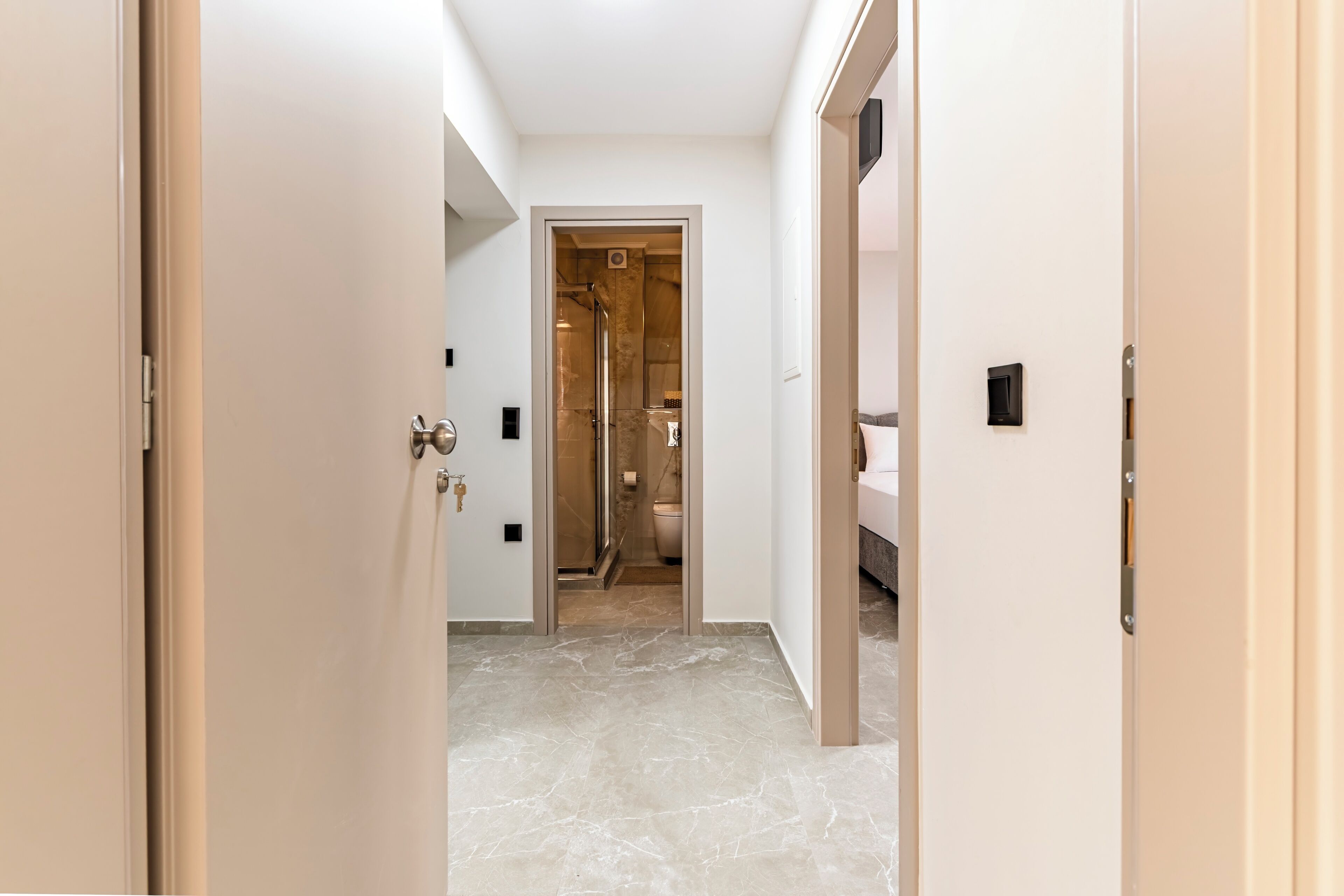 A hallway leading to a bathroom with a shower, toilet, and sink.