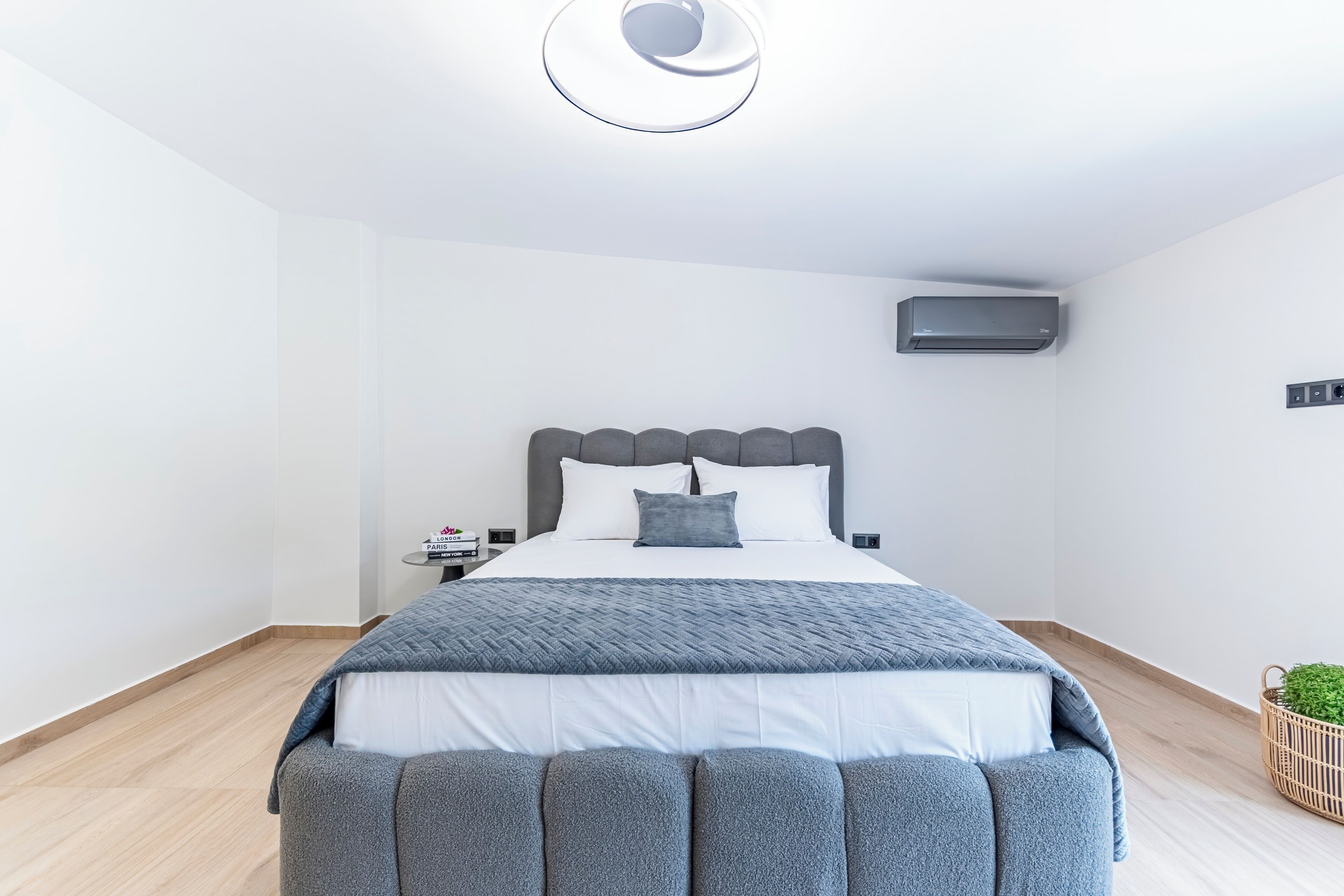 A modern bedroom with a bed, bedside table, and a wall-mounted air conditioning unit.