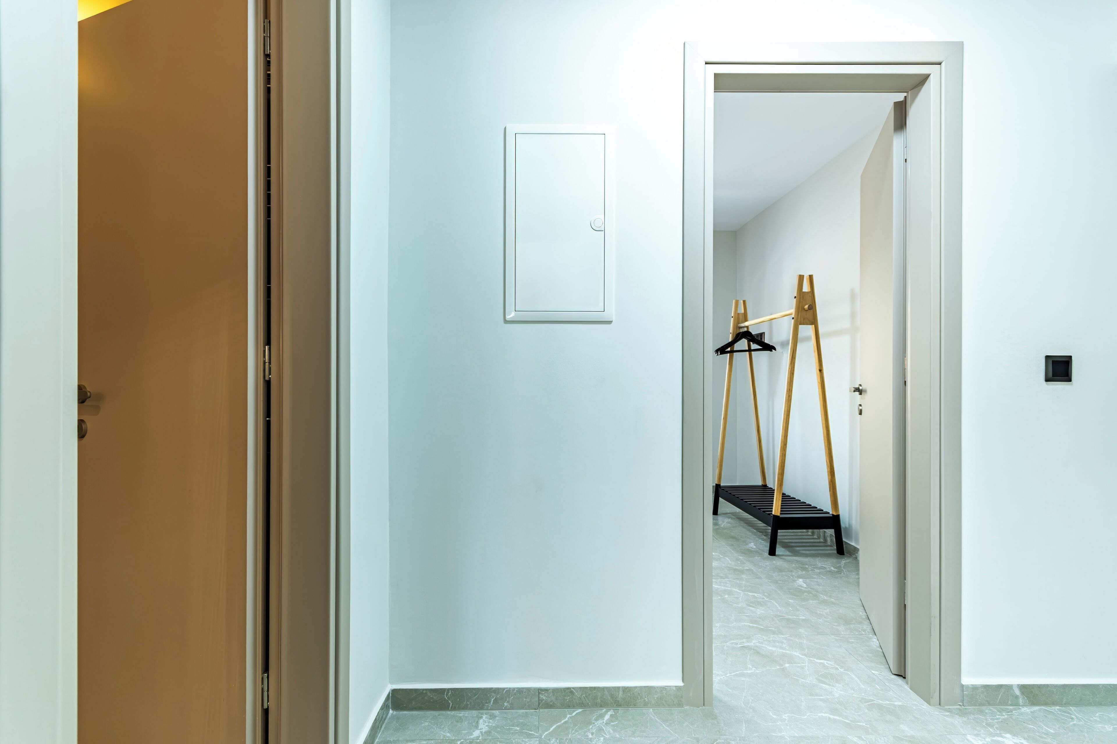 A hallway with a wooden door, a white wall, and a door with a mirror.