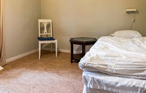 Quarto com uma cama, uma cadeira, uma mesinha e uma tomada na parede.